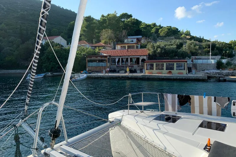 Twin Joy Yacht Photos Pics 2019 Lagoon 50 yacht docked near a scenic coastal village with lush greenery.