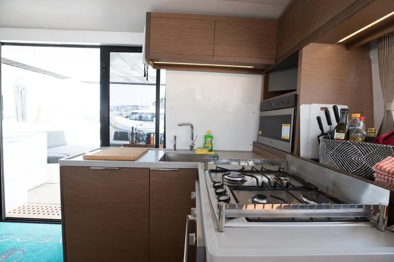 Twin Joy Yacht Photos Pics Modern kitchen interior on 2019 Lagoon 50 yacht, featuring stove, sink, and wooden cabinetry.