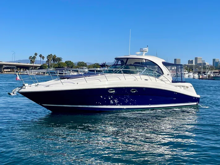 Deja Blue Yacht Photos Pics 2005 Sea Ray 390 Sundancer yacht on calm water, with cityscape and clear blue sky background.