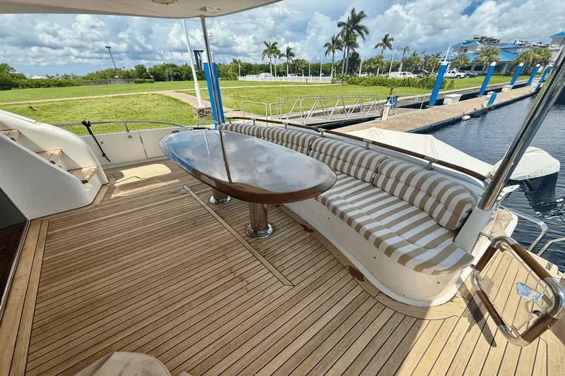 Marsha Sea Yacht Photos Pics 2005 Lazzara 68 Flybridge yacht deck with striped seating and wooden table, docked by lush greenery.