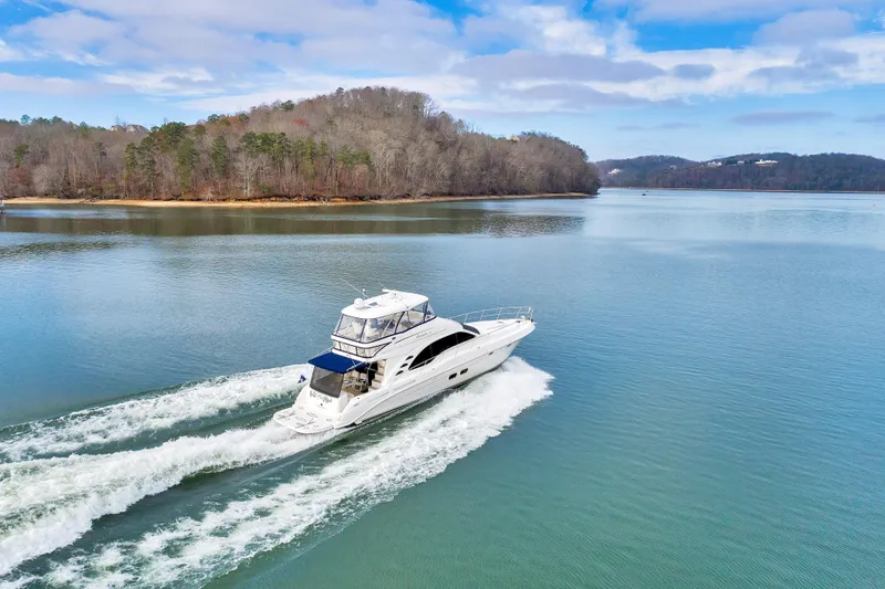  Yacht Photos Pics 2006 Sea Ray 58 Sedan Bridge yacht cruising on a serene lake with wooded shoreline.