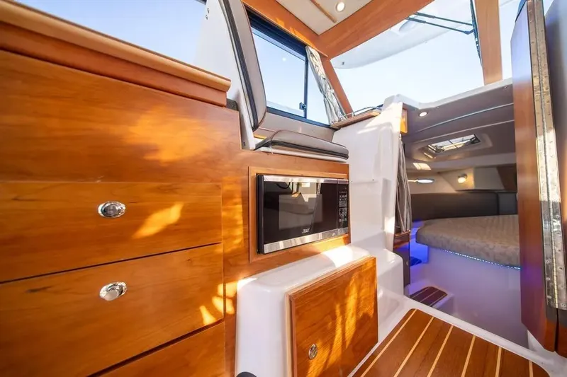  Yacht Photos Pics 2023 Cutwater C-32 Coupe interior with wood cabinetry, microwave, and cozy sleeping area.