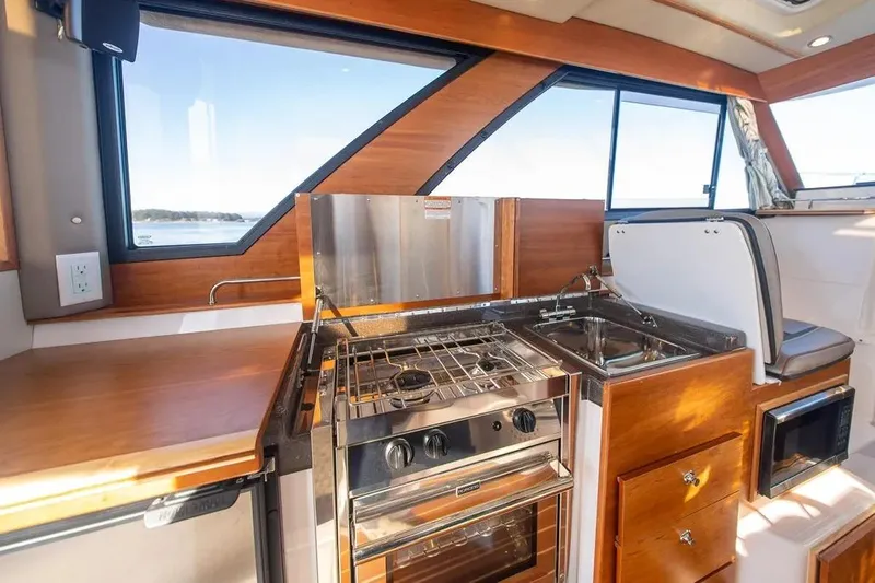  Yacht Photos Pics 2023 Cutwater C-32 Coupe interior kitchen with stove, sink, and wooden cabinetry.