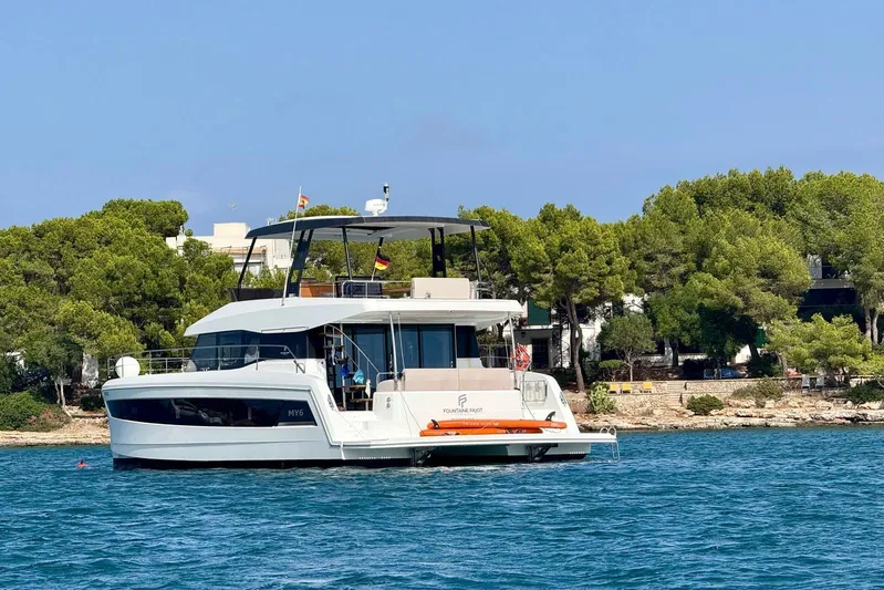  Yacht Photos Pics 2025 Fountaine Pajot MY6 yacht on serene water near a lush, tree-lined shore.