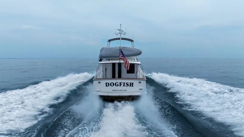 Dogfish Yacht Photos Pics 2023 Krogen Express 52 yacht cruising on open sea, rear view with American flag.