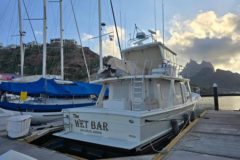 The Wetbar Yacht Photos Pics 1989 Offshore Yachts 48 Sedan docked at marina, with mountainous backdrop and cloudy sky.