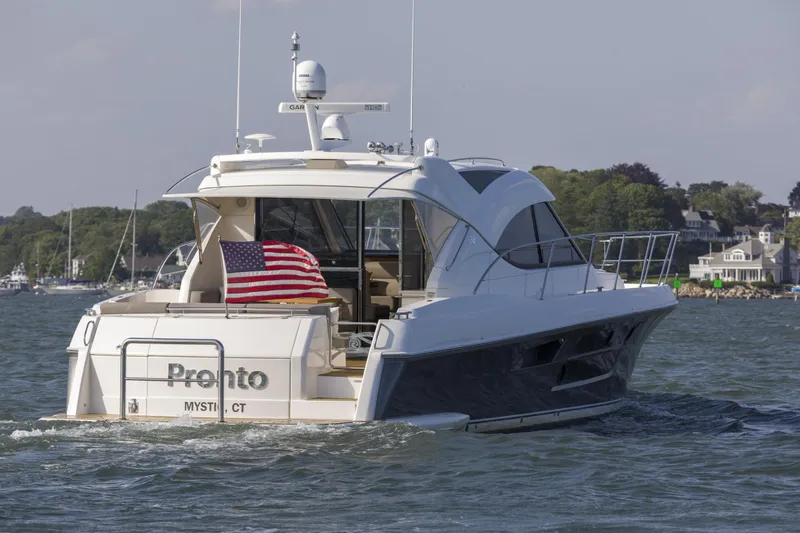 Pronto Yacht Photos Pics 2016 Riviera 5000 Sport Yacht cruising with American flag, scenic coastal background.