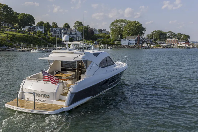 Pronto Yacht Photos Pics 2016 Riviera 5000 Sport Yacht cruising near coastal homes, displaying an American flag.