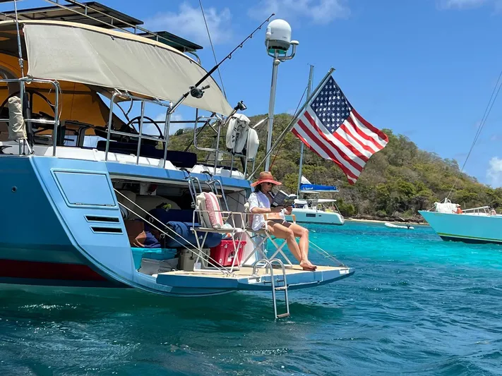 Hindsight Yacht Photos Pics 2016 Jeanneau 64 yacht with American flag, anchored in clear blue waters, person relaxing on deck.