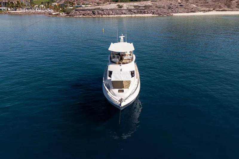 Bar&co Yacht Photos Pics 2008 Sunseeker Manhattan 73 yacht anchored in serene blue waters near a rocky coastline.