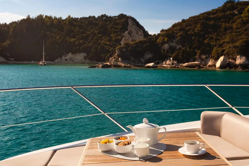 M/y Lady K Yacht Photos Pics Luxurious Sunseeker Manhattan 52 yacht with breakfast setup, overlooking serene turquoise waters and lush coastline.