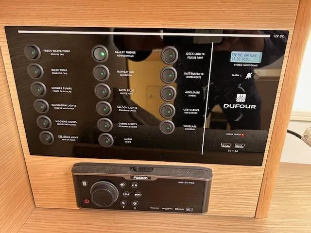 Gem Yacht Photos Pics Control panel of a 2022 Dufour 390 sailboat with various system switches and a Fusion audio unit.