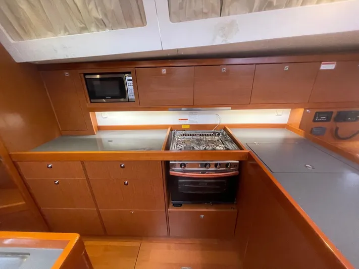 Joie De Vivre Yacht Photos Pics 2014 Beneteau Oceanis 48 yacht kitchen with stove, microwave, and wooden cabinetry.