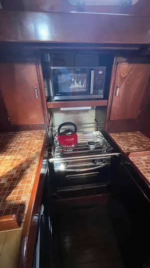 Indigo Yacht Photos Pics Galley kitchen in 1996 Amel Super Maramu-53 yacht with stove, microwave, and red kettle.