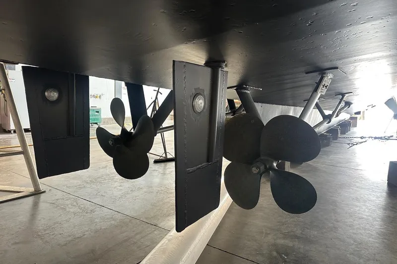 Andiamo Yacht Photos Pics Underside view of 1991 Broward 102 yacht showing propellers and rudders in a workshop.