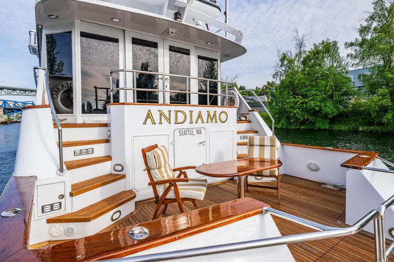 Andiamo Yacht Photos Pics Luxury yacht Broward 102, 1991 model, with elegant deck seating, docked by lush greenery.