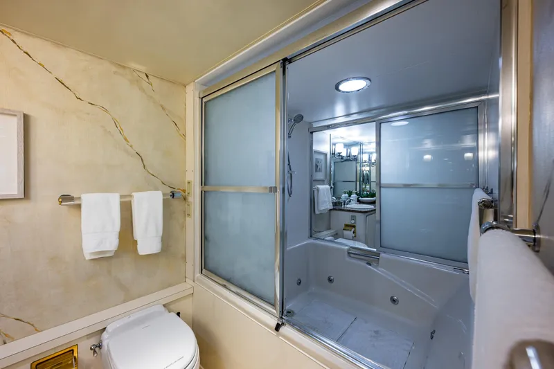 Andiamo Yacht Photos Pics Luxurious bathroom with marble walls, glass shower, and modern fixtures on a 1991 Broward 102 yacht.