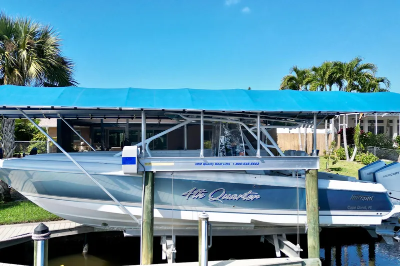  Yacht Photos Pics 2025 Intrepid 327 Cuddy boat docked under blue canopy, surrounded by tropical greenery.