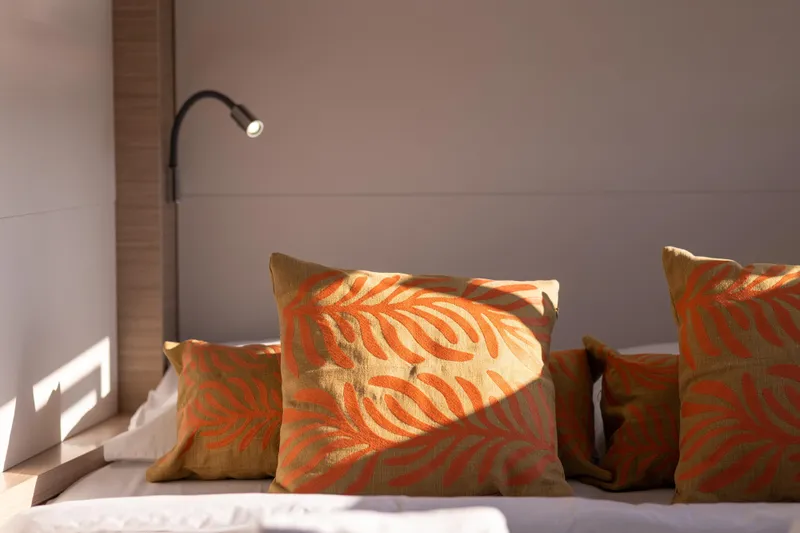 Aura Yacht Photos Pics Cozy cabin interior of 2024 Lagoon 46 yacht with decorative pillows and reading light.