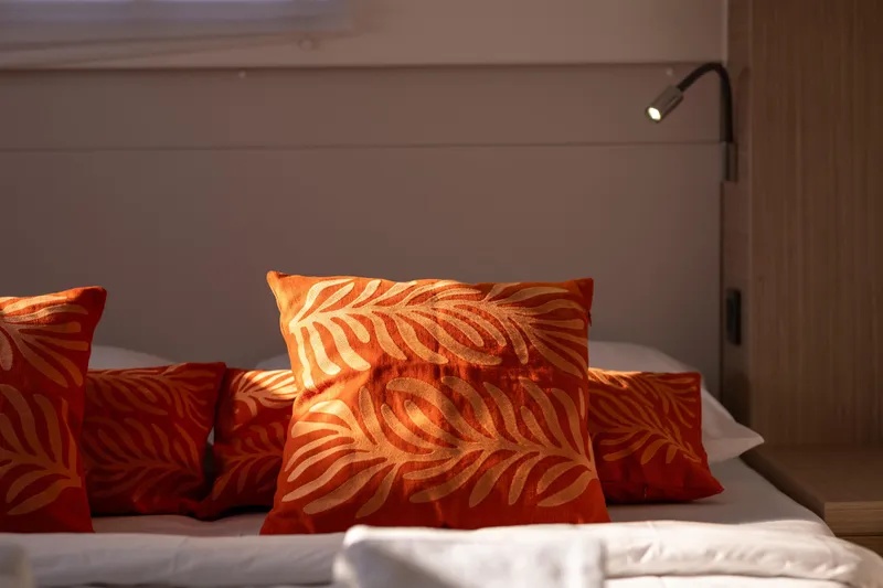 Aura Yacht Photos Pics Orange decorative pillows on a bed inside a 2024 Lagoon 46 yacht cabin.