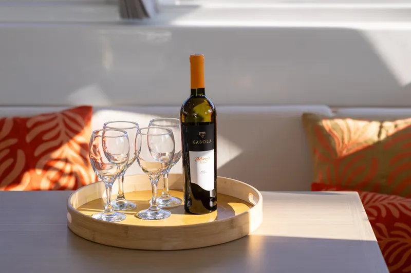 Aura Yacht Photos Pics Bottle of wine and glasses on Lagoon 46 yacht, 2024 model, with decorative cushions.