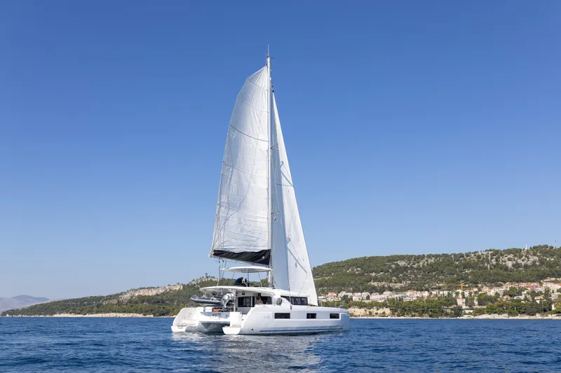 Aura Yacht Photos Pics 2024 Lagoon 46 catamaran sailing on calm sea with clear blue sky.