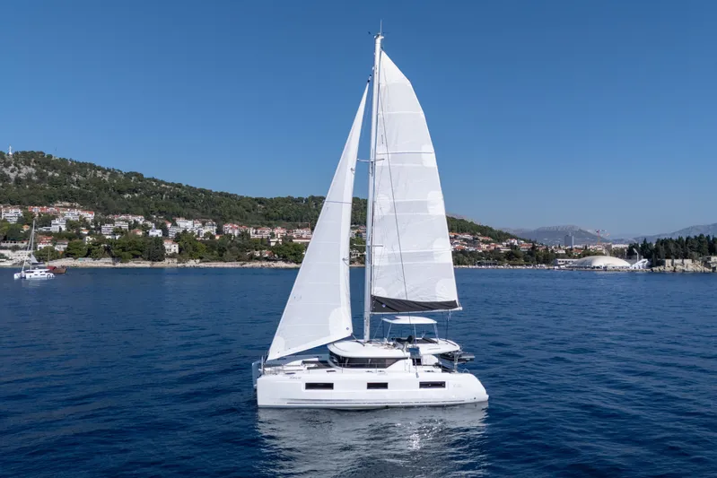 Aura Yacht Photos Pics 2024 Lagoon 46 sailing in calm waters near a scenic coastal town.