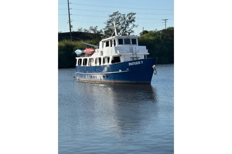 Restless T Yacht Photos Pics Blue 1971 Sermons Expedition boat "Restless T" on calm water, surrounded by greenery.