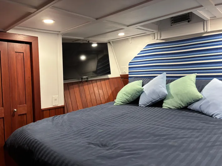 Restless T Yacht Photos Pics Cozy 1971 Sermons Expedition cabin with striped bedding, pillows, and a wall-mounted TV.