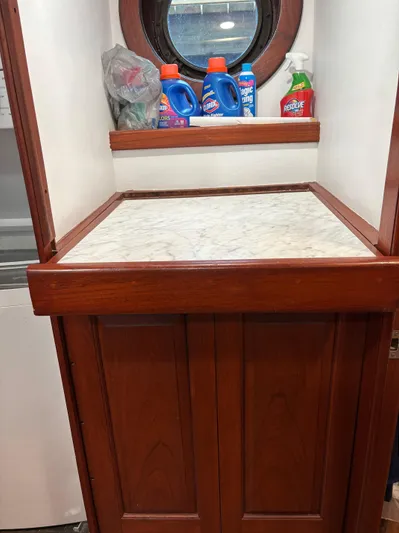 Restless T Yacht Photos Pics Wooden cabinet with cleaning supplies, porthole window, and marble countertop in a 1971 Sermons Expedition.
