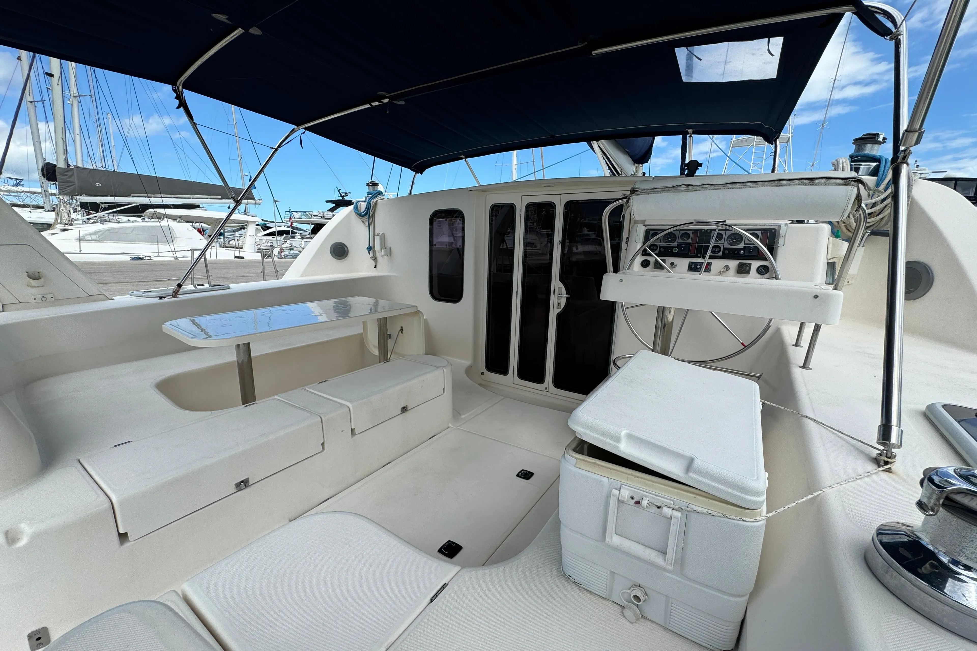 2003 Leopard 47 yacht cockpit with seating, table, and helm under a blue canopy.