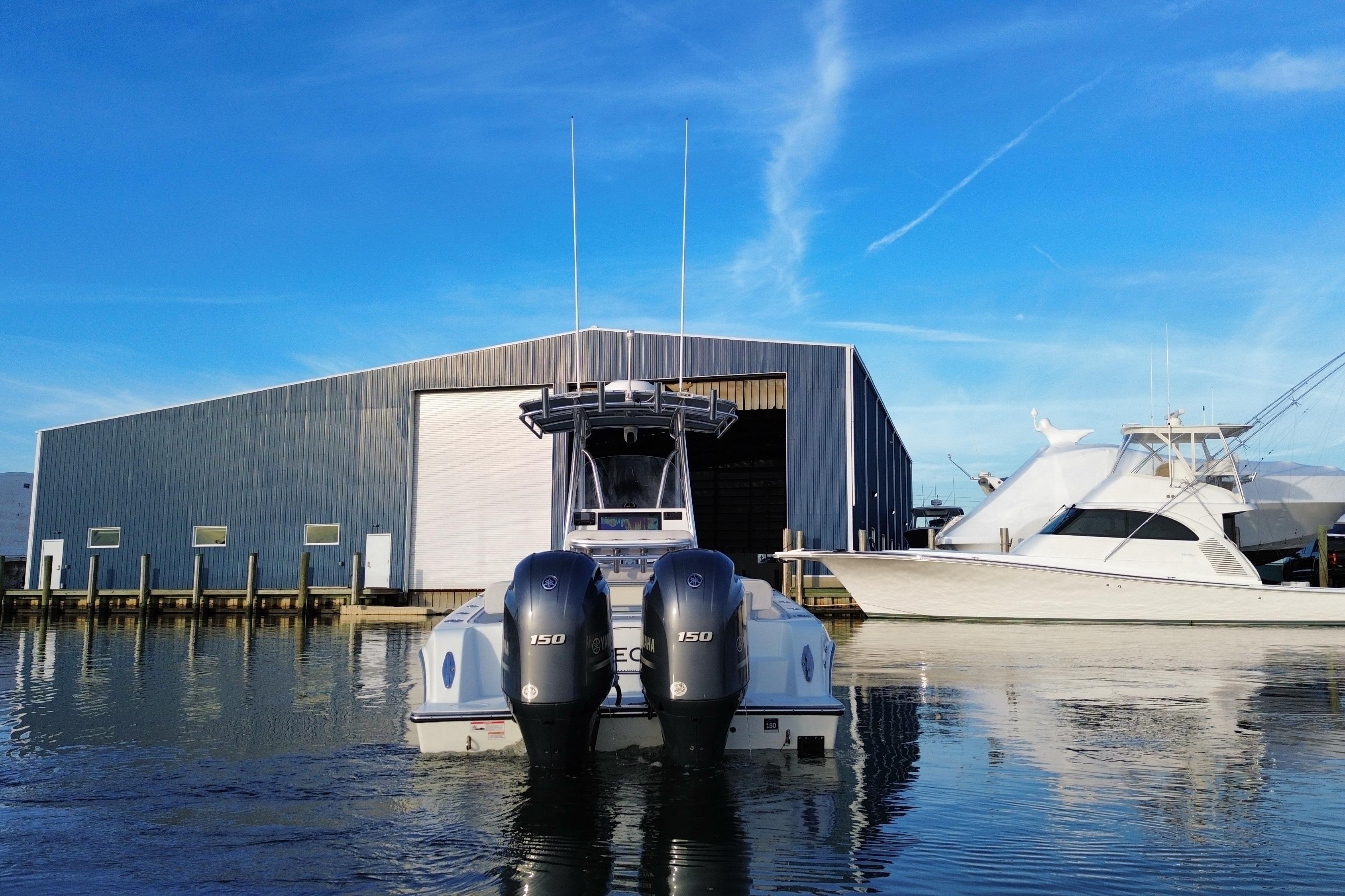 2023 Contender 24 Sport boat docked near a large warehouse, clear blue sky.