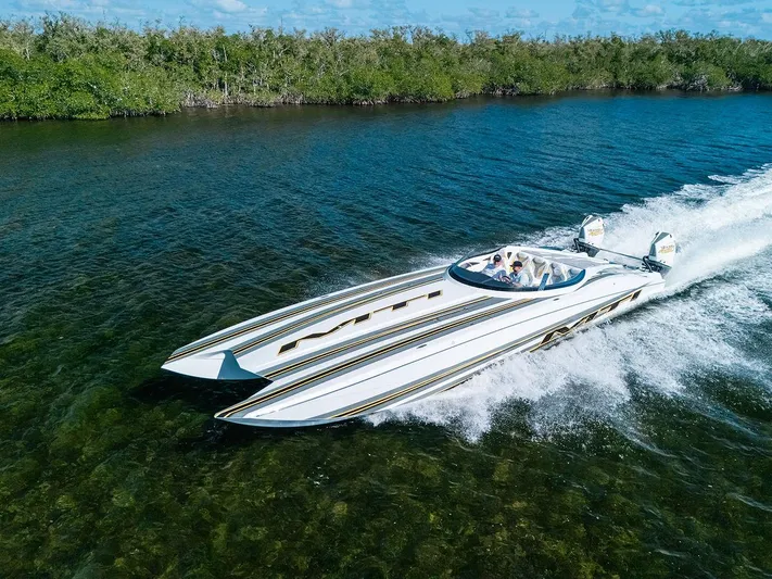  Yacht Photos Pics 2022 MTI 390X speedboat cruising on clear water near lush green shoreline.