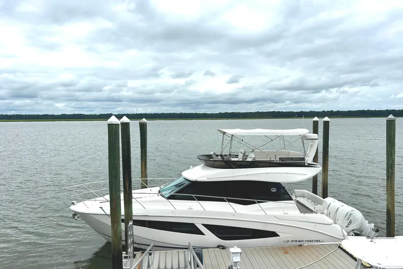 Party's Over Yacht Photos Pics 2024 Regal 42 FXO yacht docked by a serene waterfront under cloudy skies.