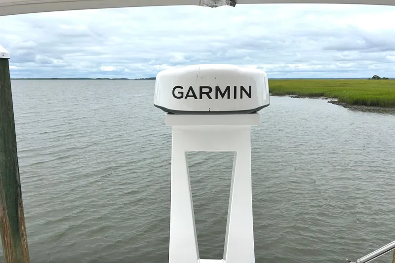 Party's Over Yacht Photos Pics Garmin radar on 2024 Regal 42 FXO boat, overlooking serene water and grassy shoreline.