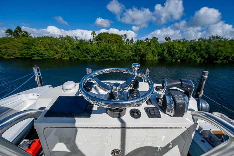  Yacht Photos Pics 2018 SeaVee 370z boat helm with steering wheel and controls, surrounded by lush greenery.