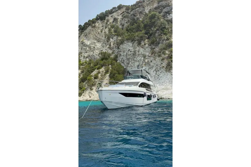  Yacht Photos Pics Azimut 68 FLY 2022 yacht anchored near rocky coastline with clear blue water.