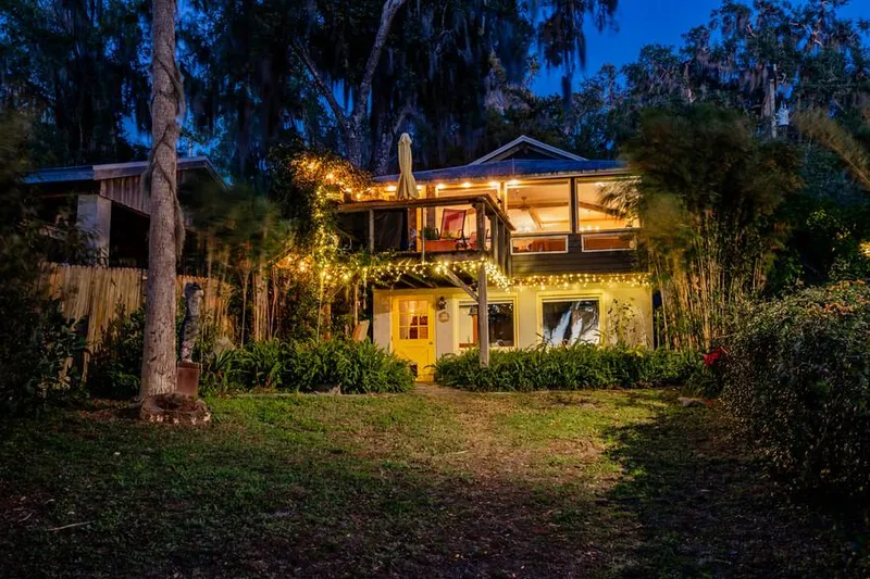 Shangri-la Yacht Photos Pics Two-story house with string lights, surrounded by trees, at dusk.