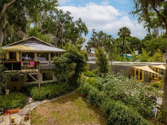 Shangri-la Yacht Photos Pics Two-story house with lush garden, surrounded by trees and greenery, under a partly cloudy sky.
