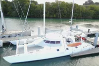 Custom 60' catamaran from 1996 docked by a lush, green shoreline.