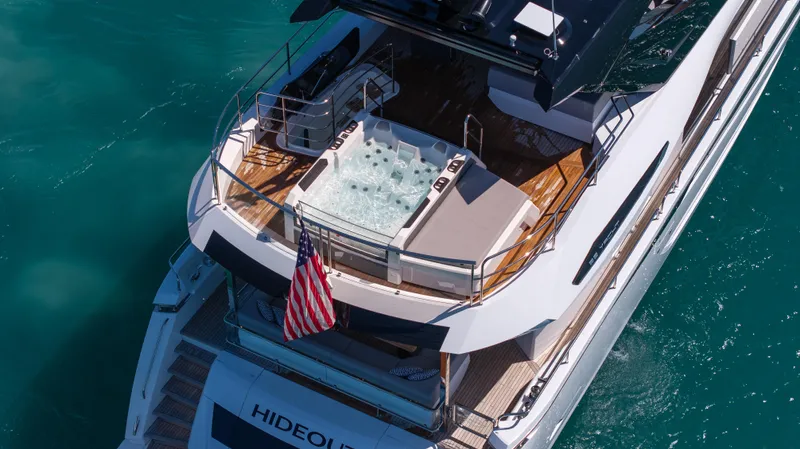 Hideout Yacht Photos Pics 2025 Sunseeker 88 Yacht with jacuzzi, American flag, and luxurious deck on turquoise water.