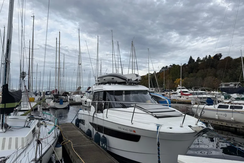  Yacht Photos Pics 2019 Jeanneau NC 895 docked in a marina, surrounded by sailboats under cloudy skies.