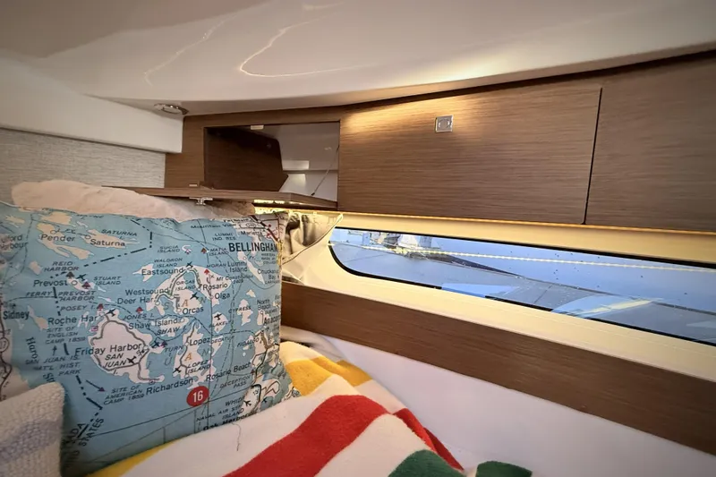 Yacht Photos Pics Interior of 2022 Jeanneau NC Weekender 895 with map-themed pillow and wooden cabinetry.