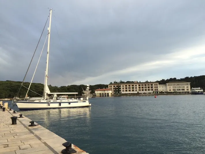 Bella Rose Yacht Photos Pics Sailboat Hallberg-Rassy 48 (2006) docked at a serene marina with buildings in the background.
