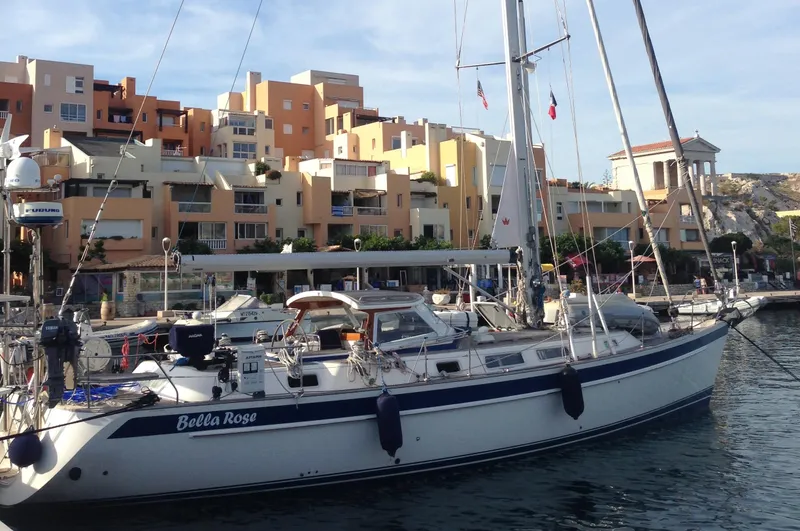 Bella Rose Yacht Photos Pics 2006 Hallberg-Rassy 48 sailboat docked in a marina with colorful buildings in the background.