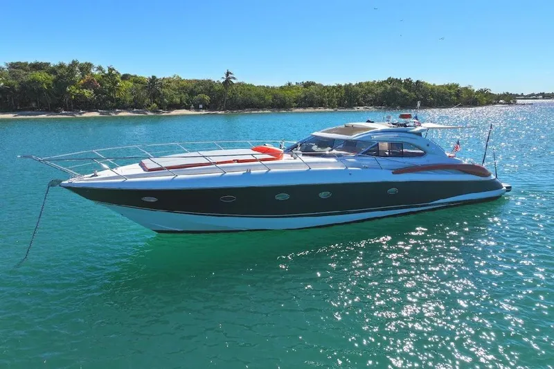  Yacht Photos Pics Sunseeker Predator 60 yacht from 2000 on clear blue water near a lush shoreline.