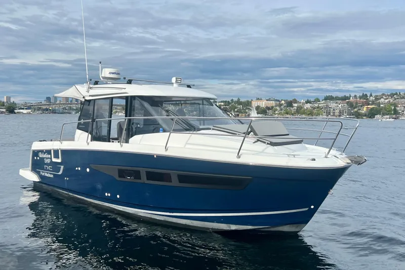  Yacht Photos Pics 2018 Jeanneau NC 895 boat on water, cityscape background, cloudy sky.