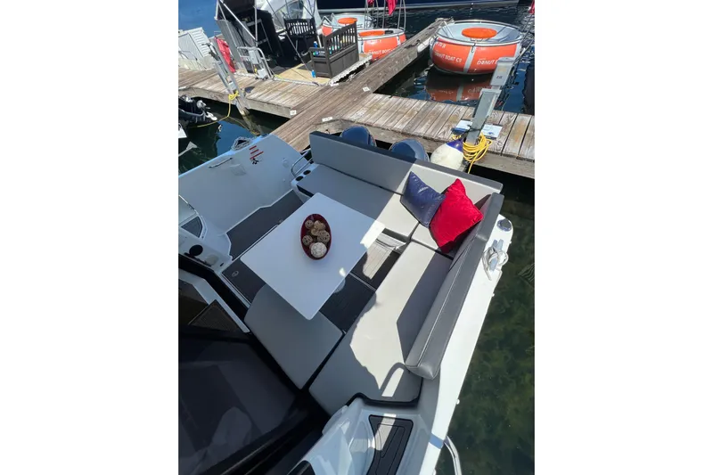  Yacht Photos Pics 2018 Jeanneau NC 895 boat with cozy seating, table, and colorful cushions at a dock.