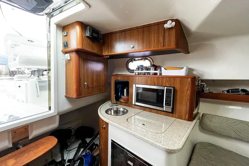 Yacht Photos Pics 2014 Pursuit OS 285 Offshore cabin with kitchenette, featuring wood cabinets, sink, and microwave.