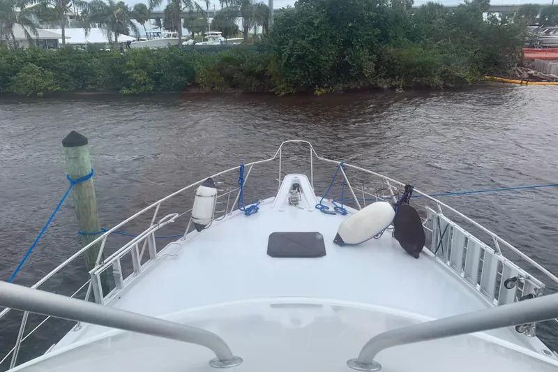 Yacht Photos Pics Bow view of 1999 Hatteras 52 Cockpit Motor Yacht docked near lush greenery.